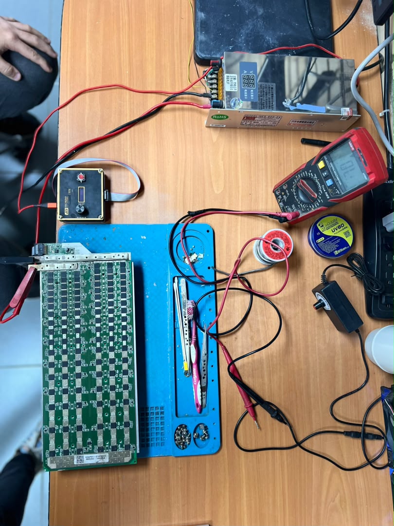 Bench power supply and multimeter wired to an ASIC hashboard and test control board for PSU diagnosis